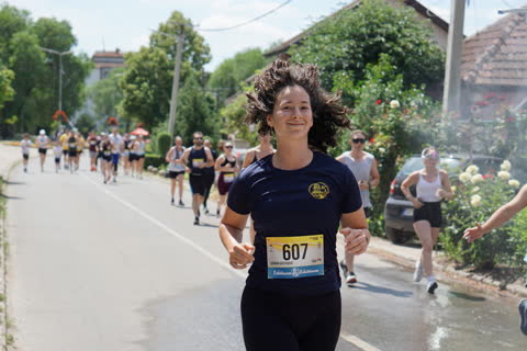 Mosolygó futónő lobogó hajjal, mögötte a teljes mezőny a fasorban