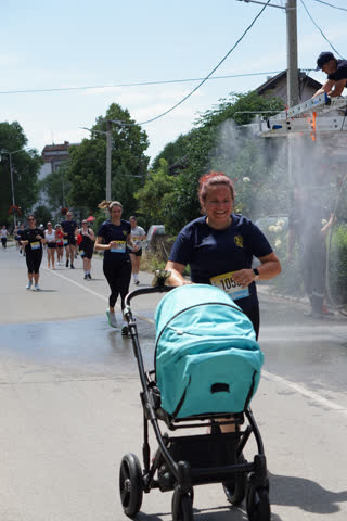 Futónő babakocsit tol, széles mosollyal, mögötte a mezőny